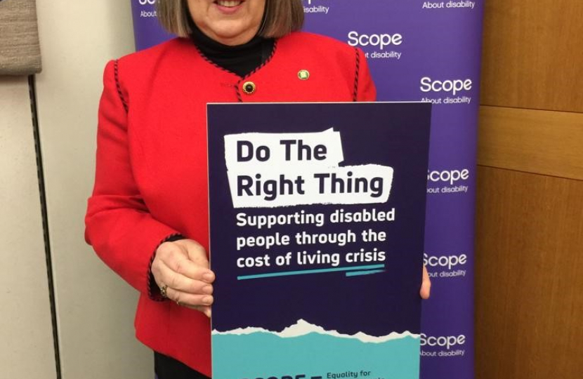 Fiona Bruce MP holding poster of Scope charity in front of Scope banner