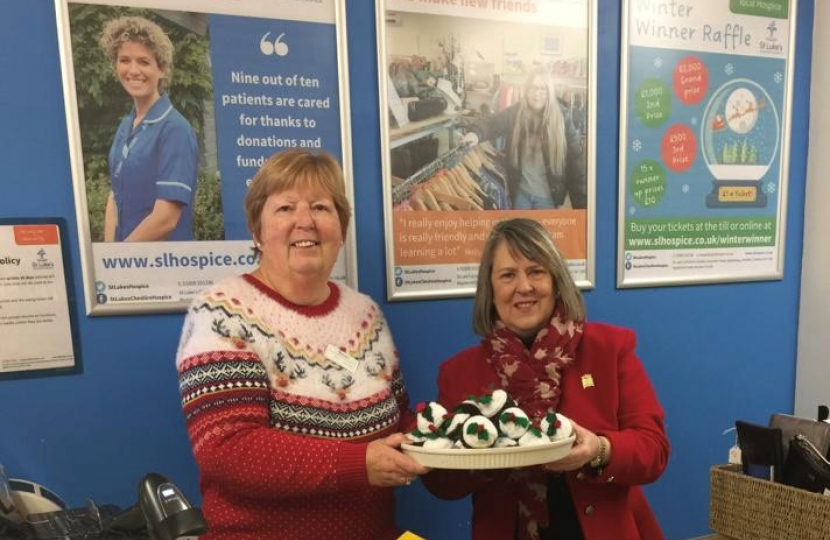 Two women holding a plate of knitted Christmas puddings behind the counter of a St Luke's Hospice shop