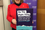 Fiona Bruce MP holding poster of Scope charity in front of Scope banner