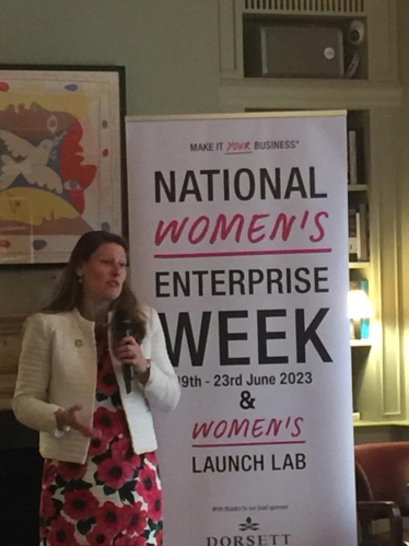 Theo Clarke MP speaking in front of a banner for National Women's Enterprise Week