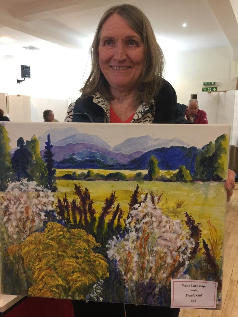 Brenda Cliff holding a colourful landscape painting