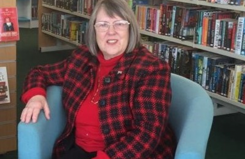 Fiona Bruce MP sitting down in a blue chair in front of library shelves