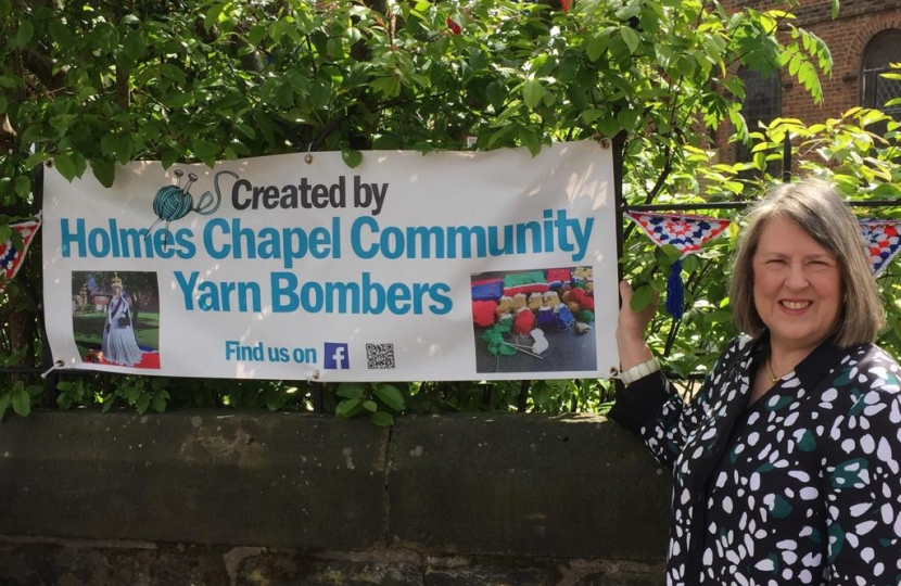 Fiona Bruce MP next to a sign for Holmes Chapel Community Yarn Bombers
