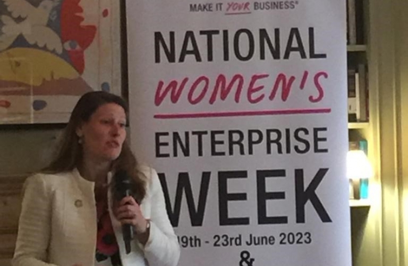 Theo Clarke MP speaking in front of a banner for National Women's Enterprise Week
