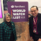 A man and woman standing in front of a World Watch List 2024 Poster