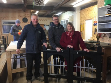 Fiona Bruce MP and two gentleman in a workshop with a pair of church gates
