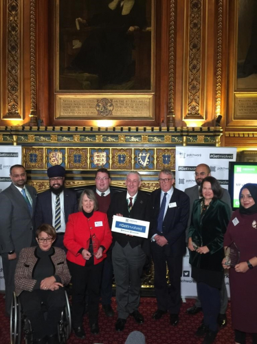 A group of people in a room in Parliament with a Patchwork Foundation logo. Some holding glass awards.